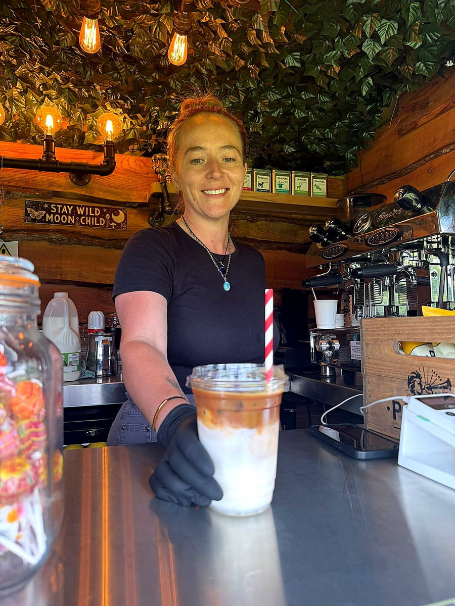 A barista passing an iced latte across the counter of the coffee van