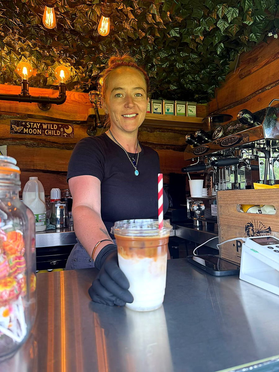 A Three Roots barista handing over an iced latte from the serving hatch of the coffee van