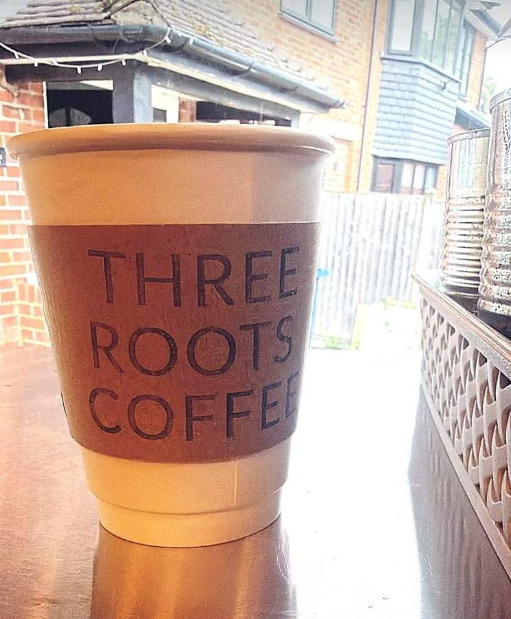 A Three Roots Coffee branded cup on the counter in the sunshine