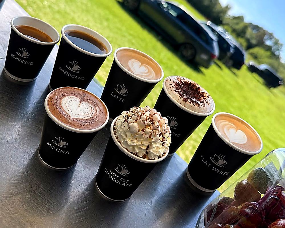 Espresso, americano, latte, mocha, cappuccino, flat white and a hot chocolate lined up on the counter in branded cups