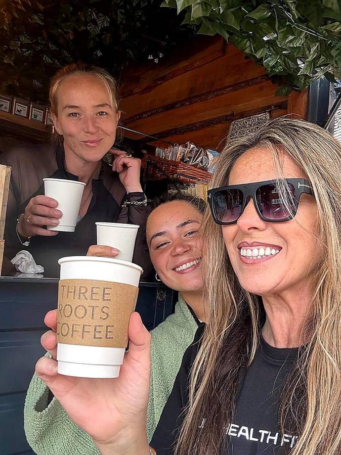 Three customers smiling with Three Roots Coffee branded cups at the van