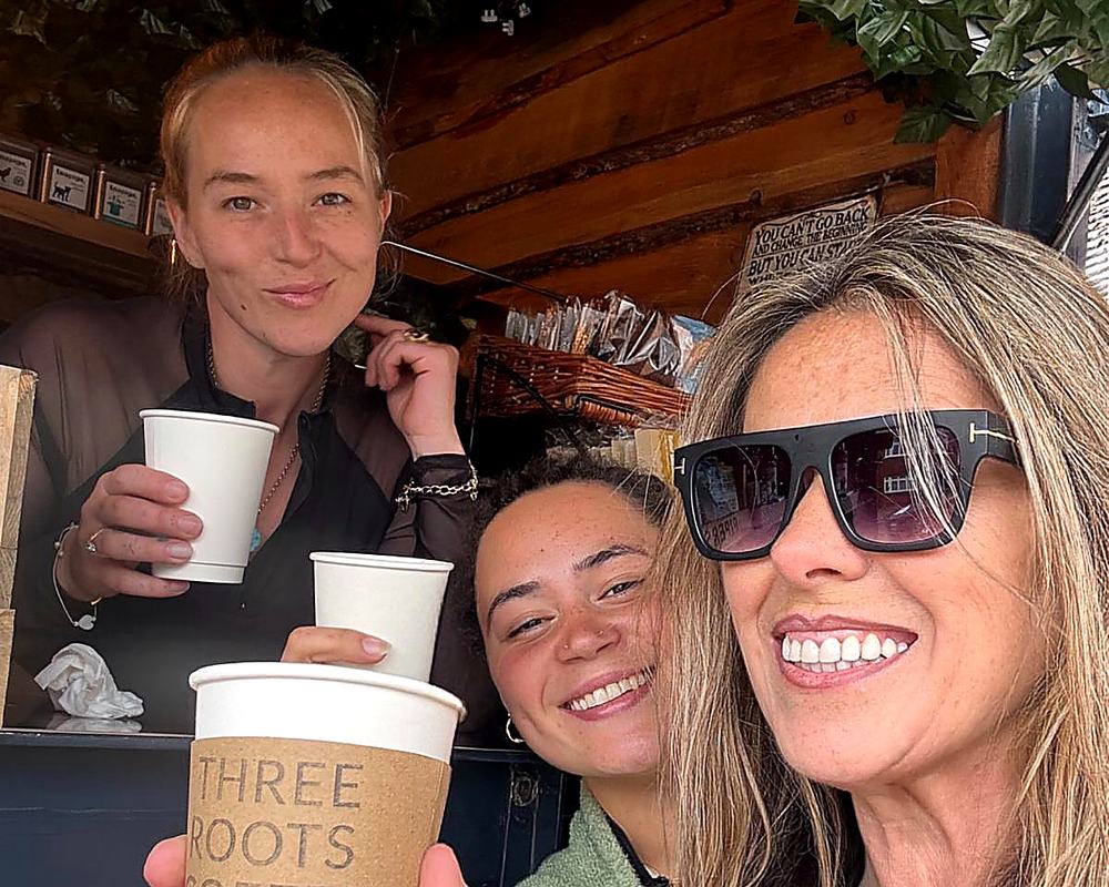 Three generations of the Three Roots family together at the serving hatch, holding branded cups