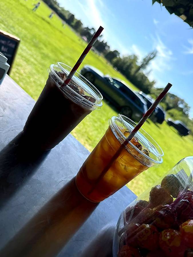 Two iced drinks side by side on the counter with a village green behind