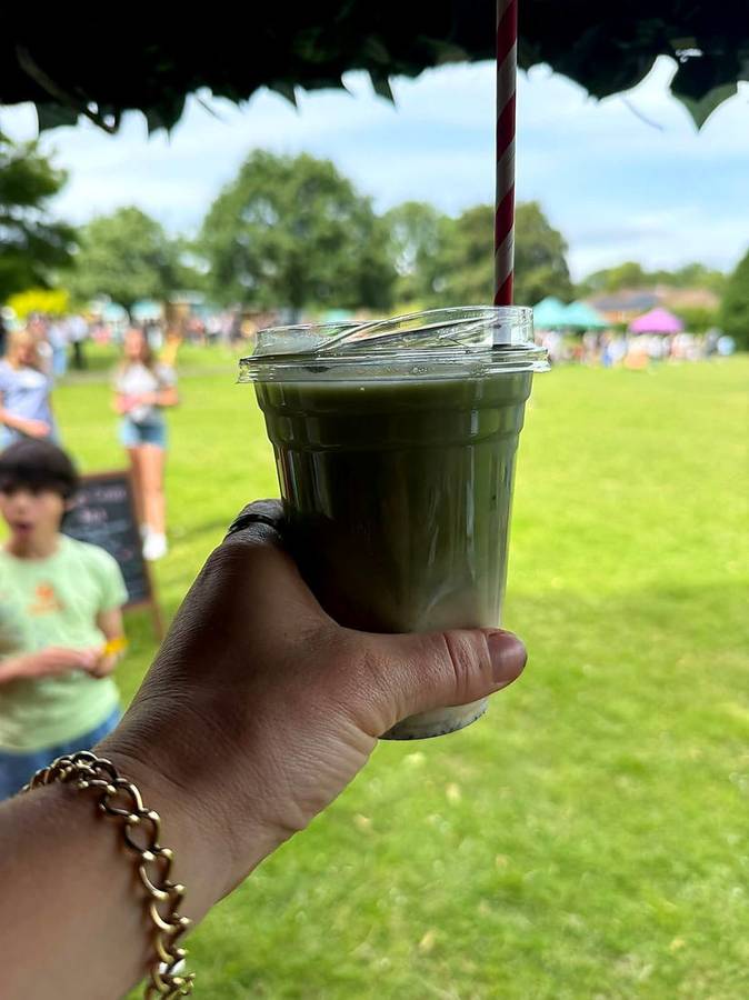 An iced matcha latte held up at an outdoor summer event