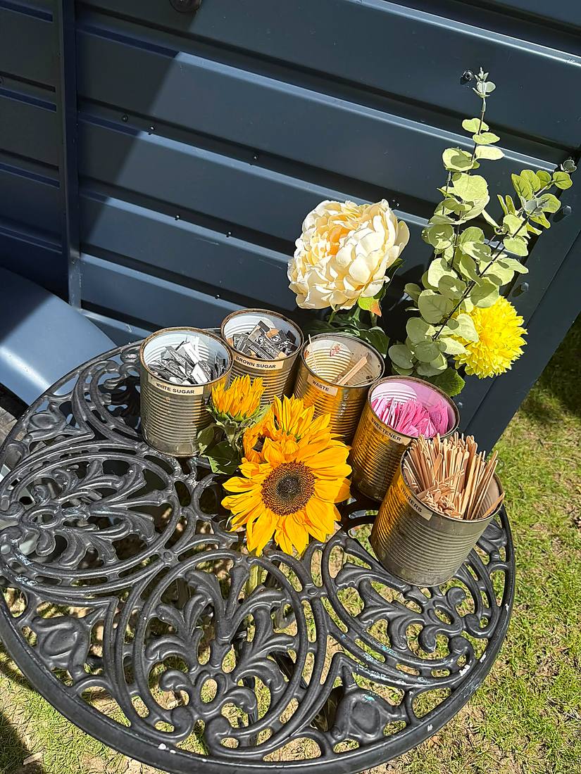 Sugar, sweetener and stirrer tins arranged with fresh sunflowers on a cast iron table beside the van