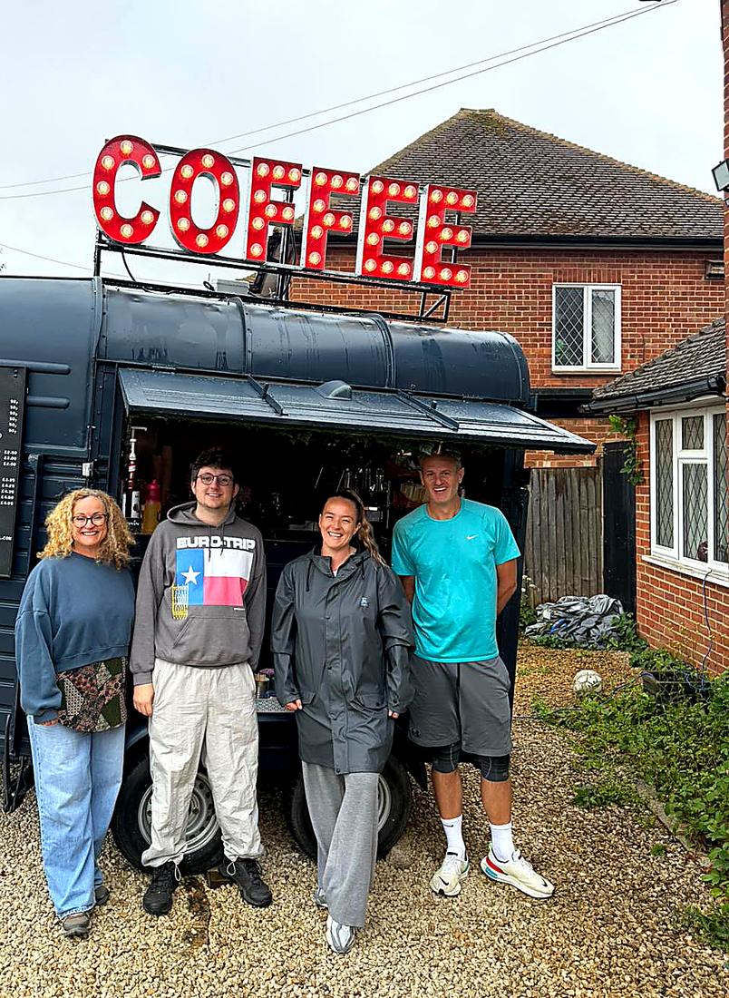 The Three Roots Coffee team together in front of the van with the lit COFFEE sign