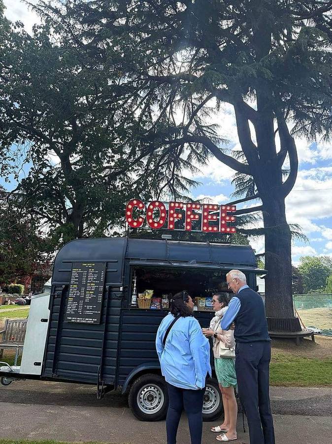 Customers being served at the coffee van under a large cedar tree