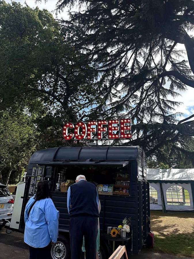 Customers being served at the van beneath a large cedar tree at an outdoor event