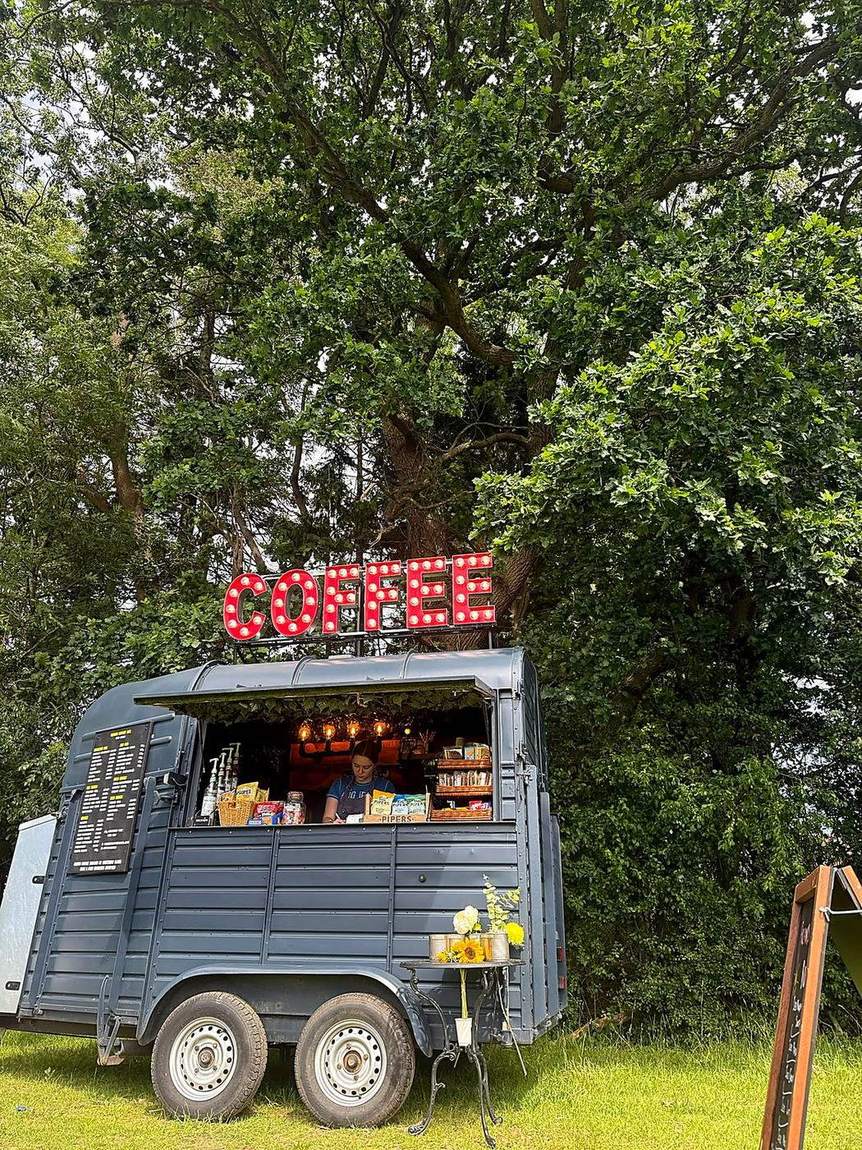 The Three Roots Coffee van parked beneath a large oak tree with the COFFEE sign lit