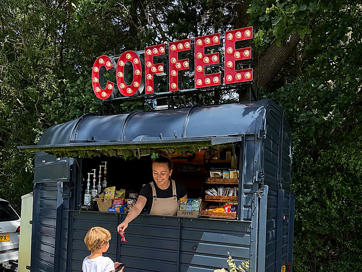 The Three Roots Coffee horsebox with its lit red COFFEE sign, a barista serving a young customer at the hatch