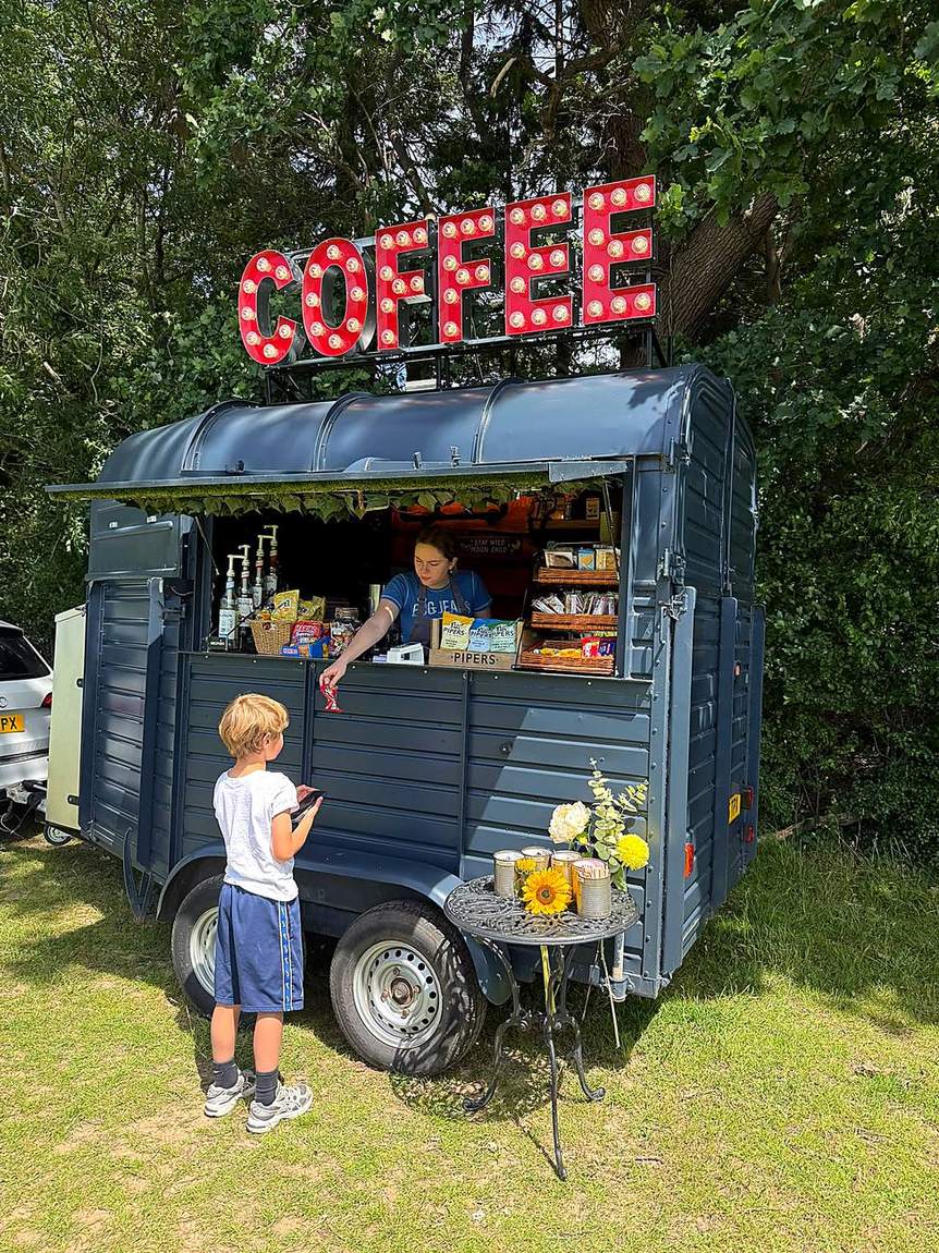 The Three Roots Coffee horsebox with its lit COFFEE sign parked on grass at a summer event